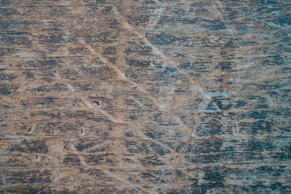 A worn hardwood floor showing scratches and dulled finish next to an unaffected section