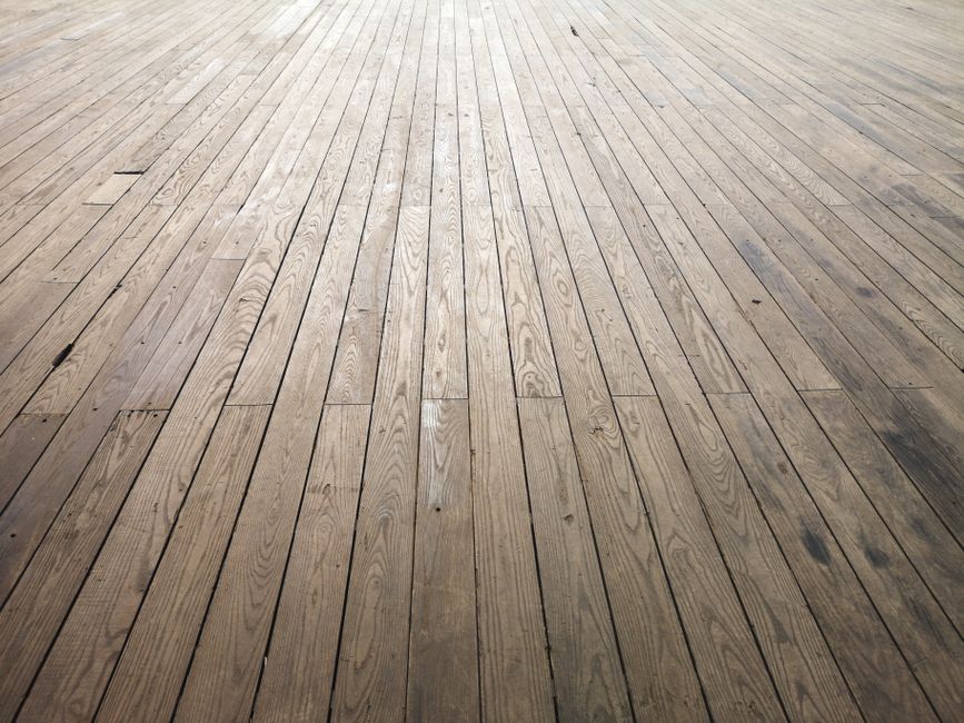 A worn, aged hardwood plank floor in need of refinishing